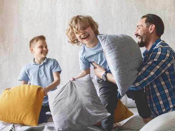 Father and two sons playing with pillows and laughing together.