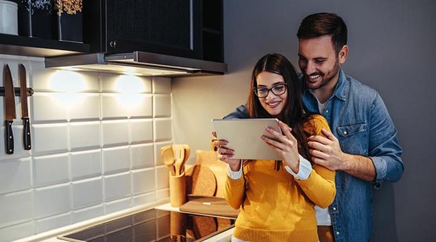 A couple in the kitchen using a tablet to browse heat pump price plans.